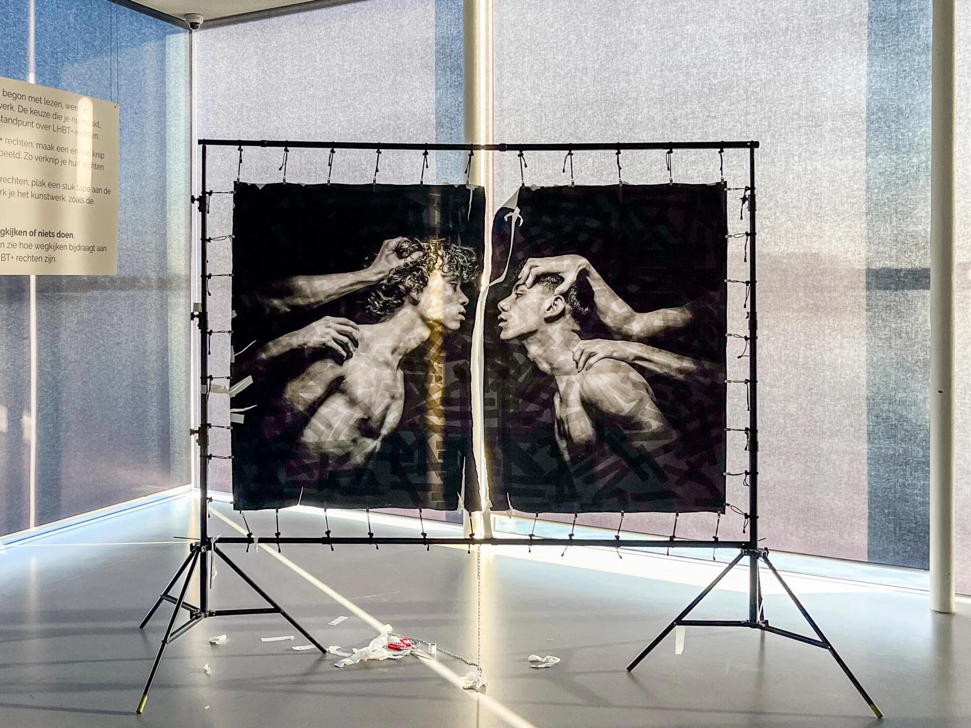 A large-format monochrome artwork by Arjan Spannenburg, RESTRAINT, sits vandalized with a central tear on a metal frame at Kunstlinie Almere.