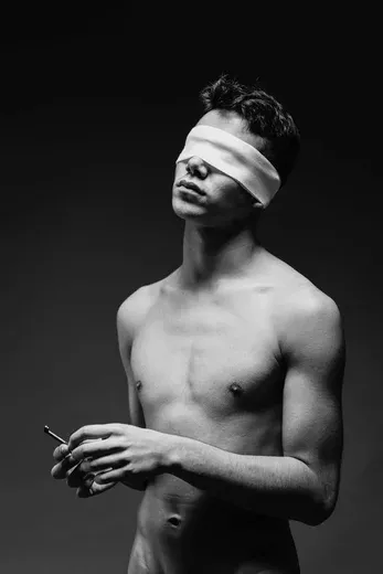 A black and white conceptual portrait of a blindfolded man holding a key.