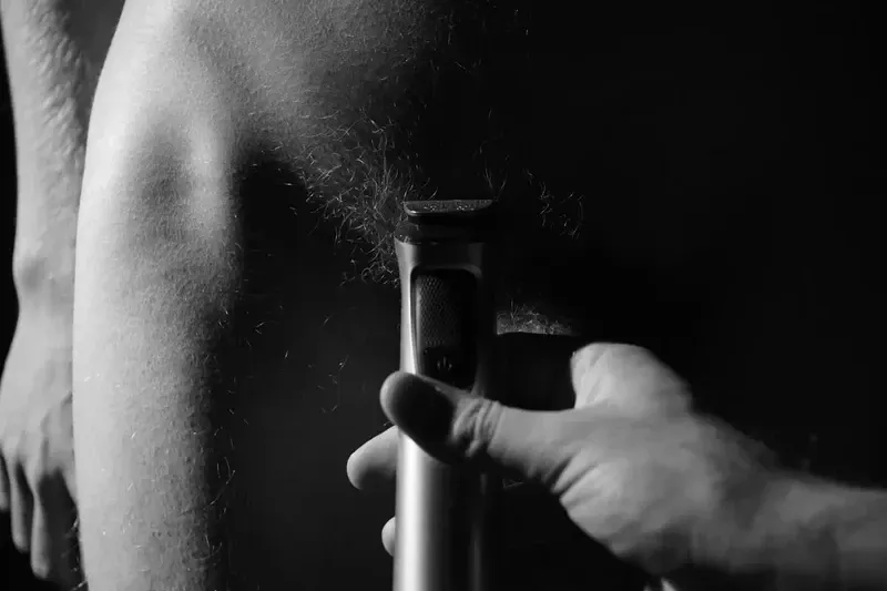 B/W art: Hand holds electric razor to shave body hair. Close-up, intimate.