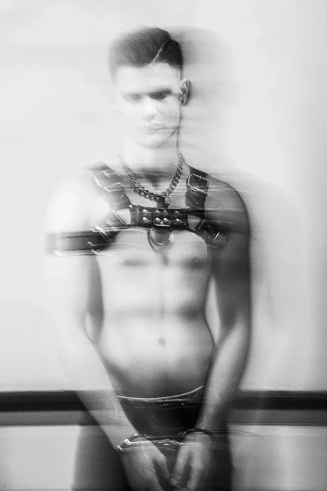 Abstract black and white fine art portrait 'CONFUSED' by Arjan Spannenburg, featuring a man in a leather harness and handcuffs dissolving into motion blur.