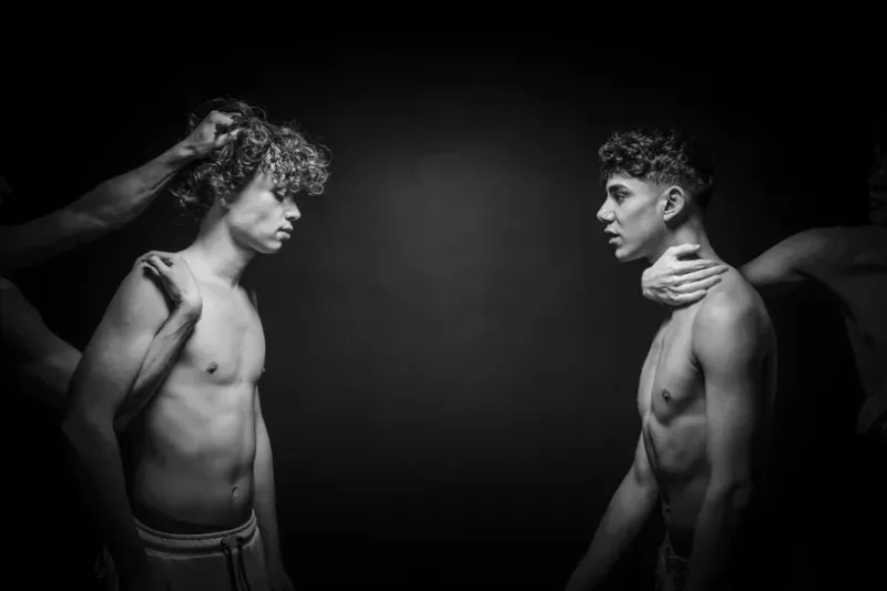 Black and white fine art photography titled Restraint I showing two men controlled by external hands in a dark space.