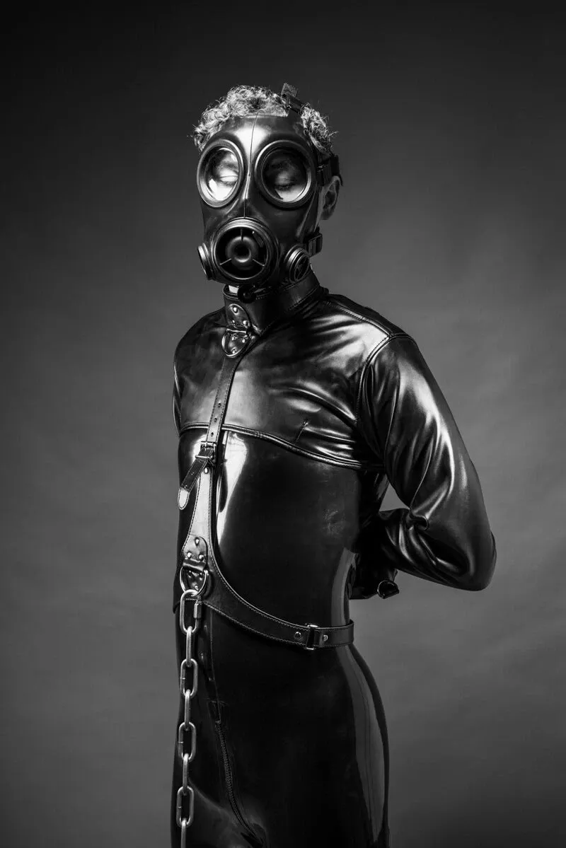 Fine art photograph titled "WHERE IT CALMS" by Arjan Spannenburg is a black and white fine art photograph of a person in a latex suit and gas mask, exploring themes of queer identity and sensory deprivation.